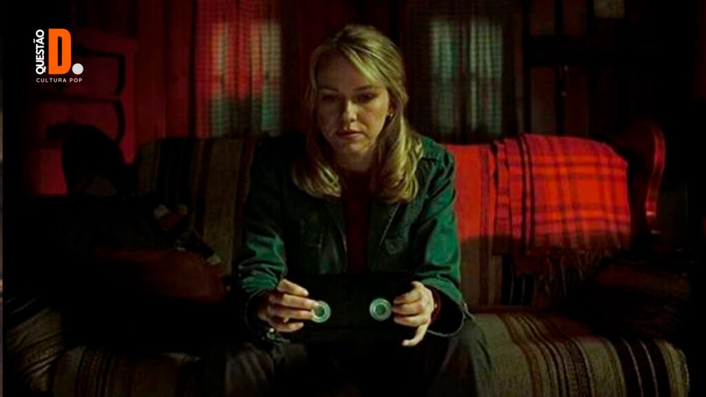Maldição? Já era | Naomi Watts sentando em segurando uma fita VHS, em um cenário escuro | Questão D