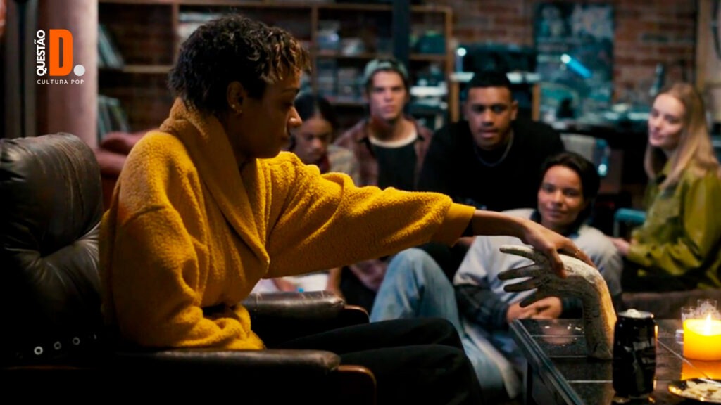 Madição? Já Era | Cena de Sophie Wilde segurando um mão embalsamada. Atrás dela tem um grupo de adolescentes assistindo tudo | Questão D